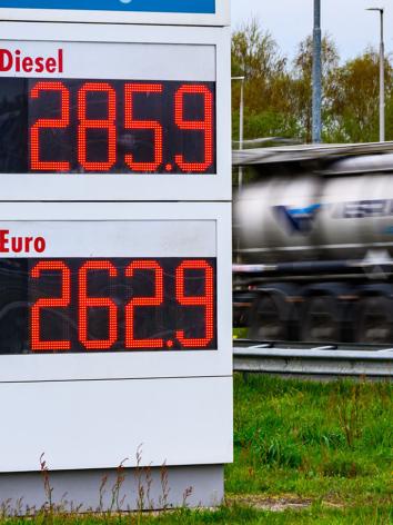 Brandstofprijzen op een bord van een tankstation (2,85 voor Diesel en 2.62 voor Benzine) met een langsrijdende vrachtwagen