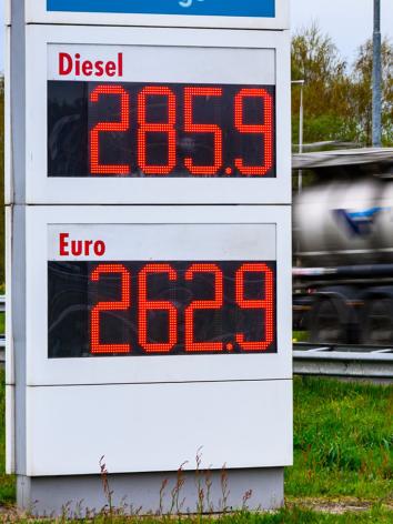 Brandstofprijzen op een bord van een tankstation (2,85 voor Diesel en 2.62 voor Benzine) met een langsrijdende vrachtwagen