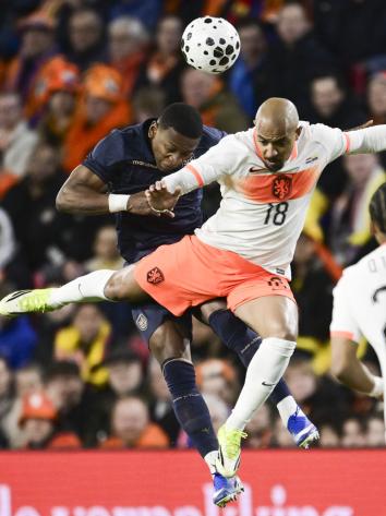 Twee voetballers doen een kopduel. Een voetballer draagt het uitshirt van het Nederlands elftal en de ander het thuisshirt van Ecuador.