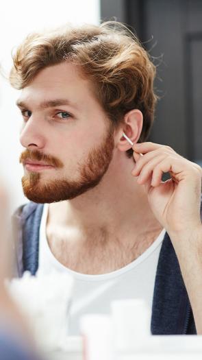 Man met baard kijkt in de spiegel en maakt zijn oor schoon met een wattenstaafje
