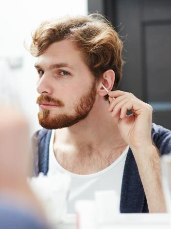 Man met baard kijkt in de spiegel en maakt zijn oor schoon met een wattenstaafje