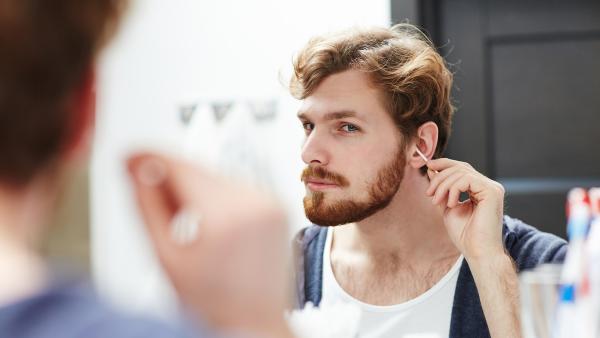 Man met baard kijkt in de spiegel en maakt zijn oor schoon met een wattenstaafje
