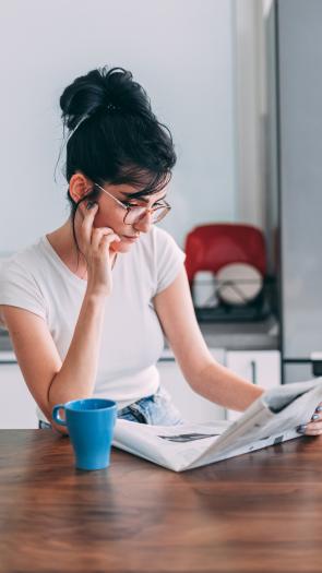 Vrouw leest krant met kop koffie zittend aan tafel in een keuken 