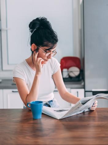 Vrouw leest krant met kop koffie zittend aan tafel in een keuken 