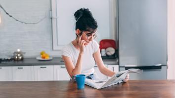Vrouw leest krant met kop koffie zittend aan tafel in een keuken