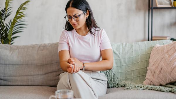 Vrouw krabt aan haar arm met een gefronst gezicht terwijl ze op de bank zit