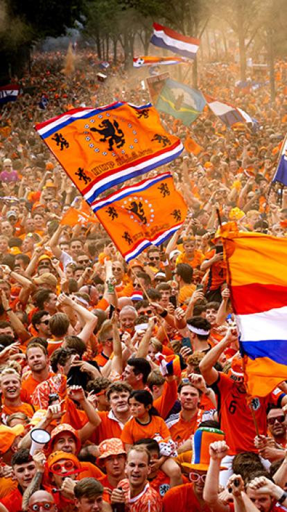 Straat gevuld met mensen in oranje kleding met verschillende Nederlandse vlaggen