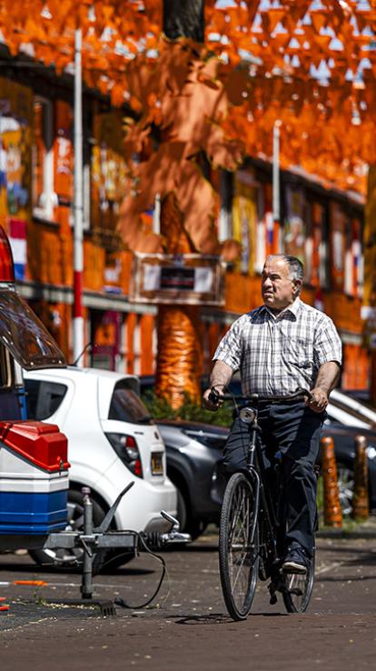Man fietst door een straat die helemaal is versierd met oranje vlaggetjes en Nederlandse vlaggen.