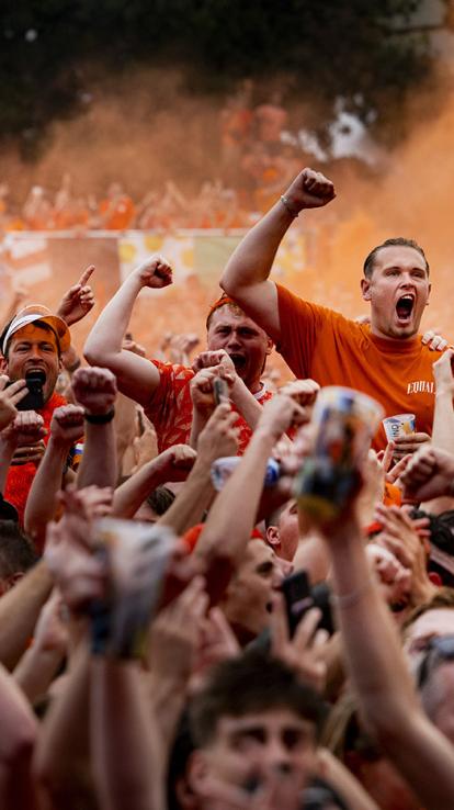 Groep mannen in oranje kleding juichen uitbundig. Diverse mannen zitten op elkaar schouders en er worden vuisten in de lucht gestoken.
