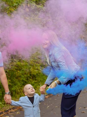 Jong gezin blaast roze en blauwe rook als genderreveal in de lucht