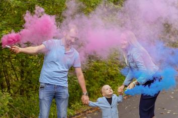 Jong gezin blaast roze en blauwe rook als genderreveal in de lucht