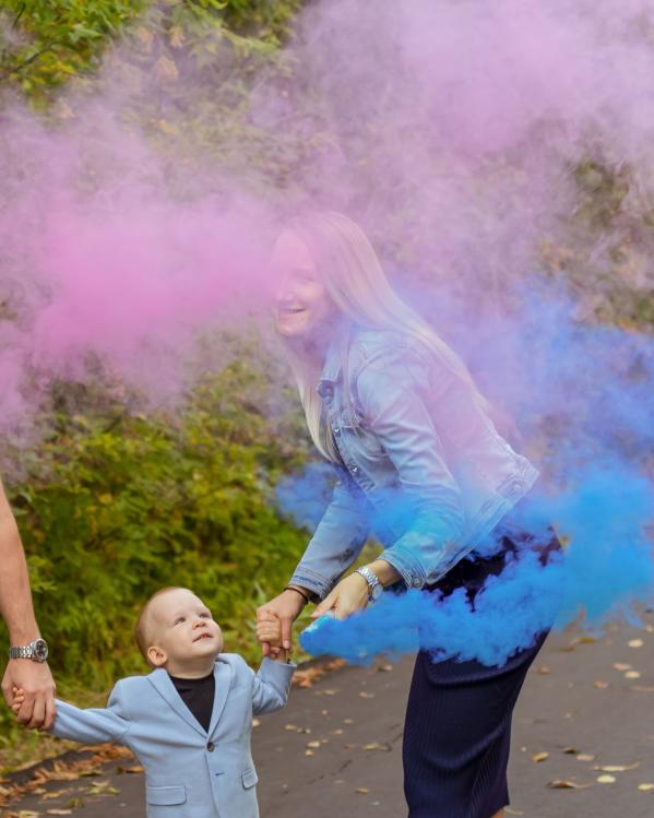 Jong gezin blaast roze en blauwe rook als genderreveal in de lucht