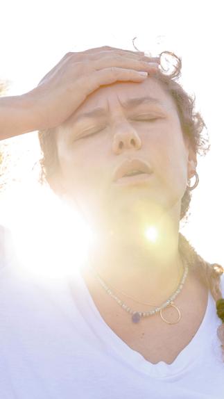 Een vrouw heeft last van de hitte en legt een hand op haar hoofd, met een felle zon achter haar