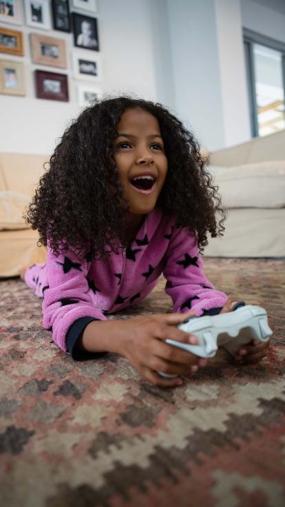 Een meisje ligt op de grond te gamen met een videogame-controller in haar handen