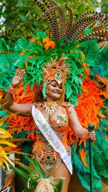 Vrouw in kostuum voor zomercarnaval met veren hoofdstuk en verenkrans om haar heen kijkt lachend en zwaaiend om zich heen