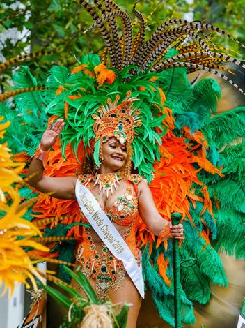 Vrouw in kostuum voor zomercarnaval met veren hoofdstuk en verenkrans om haar heen kijkt lachend en zwaaiend om zich heen