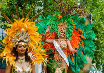 Vrouw in kostuum voor zomercarnaval met veren hoofdstuk en verenkrans om haar heen kijkt lachend en zwaaiend om zich heen