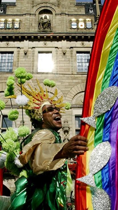 Man in kostuum waar bomen en wolken om hem heen zweven met kroon op zijn hoofd en glittervissen in zijn handen danst lachend tussen regenbogen gemaakt van stof.