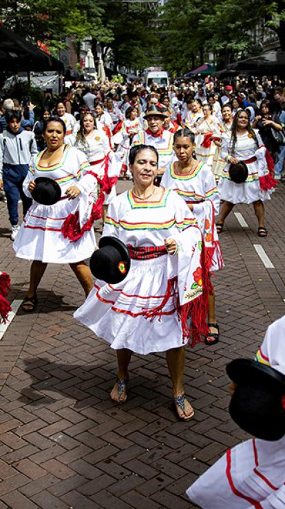 Groep vrouwen danst op straat in traditionele klederdracht met bolhoedjes in hun handen