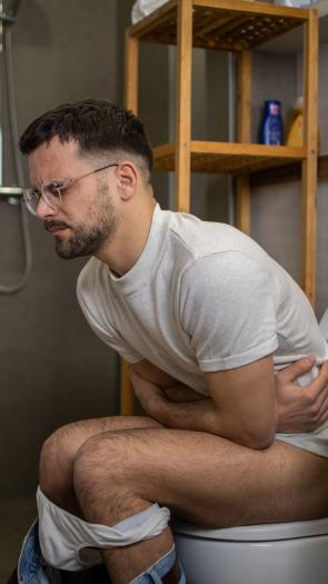 Een man zit met buikpijn op het toilet