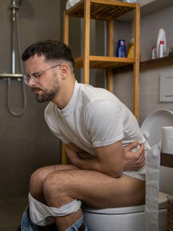 Een man zit met buikpijn op het toilet