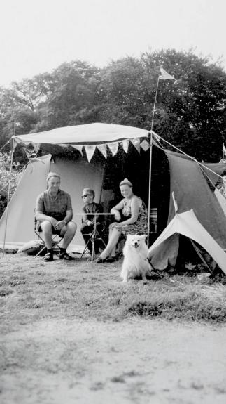 Een zwart-witfoto van een gezin met hond die voor hun tent zitten
