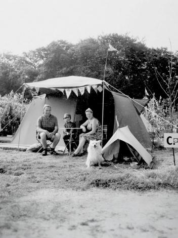 Een zwart-witfoto van een gezin met hond die voor hun tent zitten
