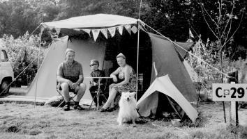 Een zwart-witfoto van een gezin met hond die voor hun tent zitten