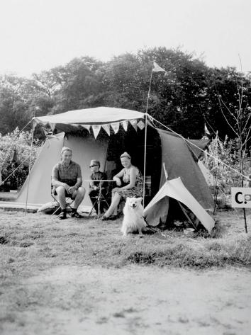 Een zwart-witfoto van een gezin met hond die voor hun tent zitten