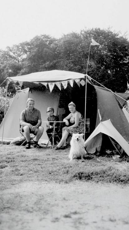 Een zwart-witfoto van een gezin met hond die voor hun tent zitten