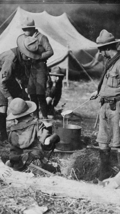 Nederlandse padvinders kamperen op een landgoed. Op de voorgrond gieten ze eten in de pan; op de achtergrond zie je een tent staan.
