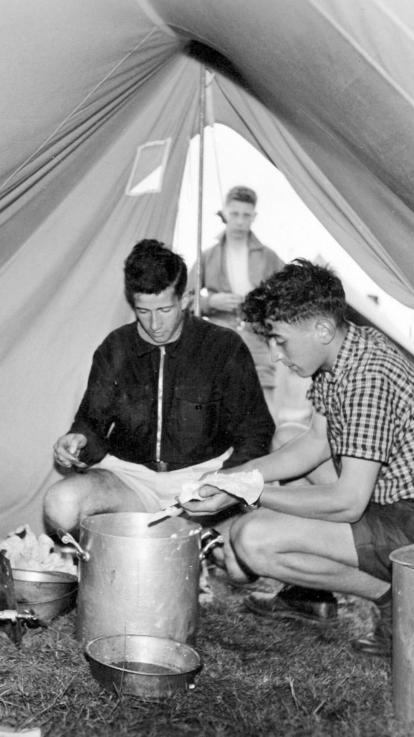 Zwart-witfoto van jongeren in hun tent met een pan eten