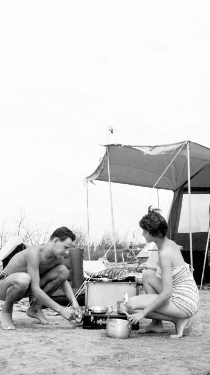 Een zwart-witfoto van een kamperend stel voor hun tent met een 'keukentje' in de weer