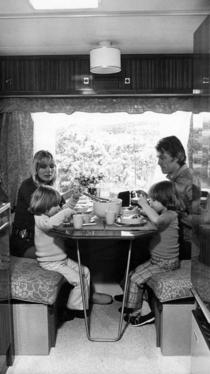 een zwart-witfoto van een kamperend gezin die aan het eten is in de caravan