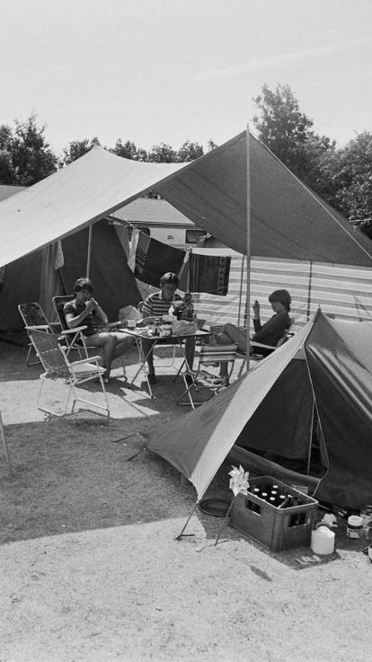 Zwart-witfoto van verschillende tenten op een camping, met mensen buiten en bierkratjes voor de tent