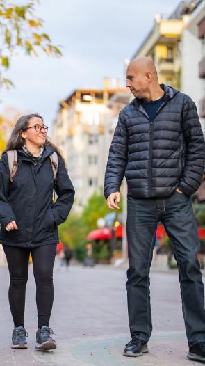 drie mensen lopen samen over straat, onder wie één erg lange man