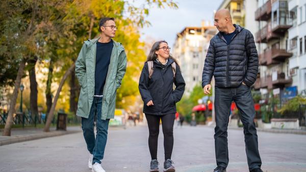 drie mensen lopen samen over straat, onder wie één erg lange man