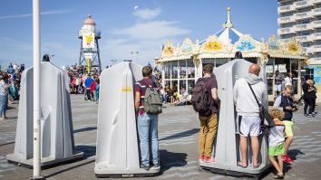 Op de scheveningse boulevard staan urinoirs waar 3 mannen aan het plassen zijn. Daarnaast lopen kindjes. 