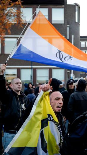 Iemand zwaait met de prinsenvlag bij een anti-azcdemonstratie