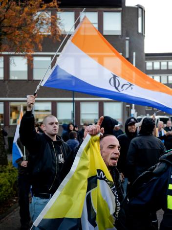 Iemand zwaait met de prinsenvlag bij een anti-azcdemonstratie