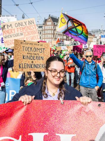Deelnemers aan de Feminist March lopen door het centrum van Amsterdam met borden en doeken