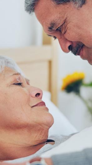 Een vrouw ligt ziek in bed; haar man buigt over haar heen en kijkt haar aan