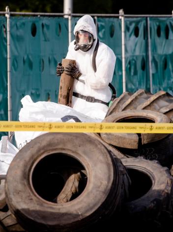 Iemand in een beschermend pak ruimt asbest op bij gedumpt afval op een snelweg
