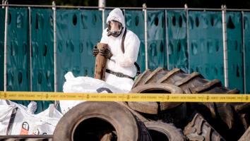 Iemand in een beschermend pak ruimt asbest op bij gedumpt afval op een snelweg