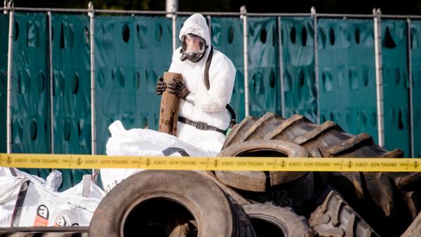 Iemand in een beschermend pak ruimt asbest op bij gedumpt afval op een snelweg