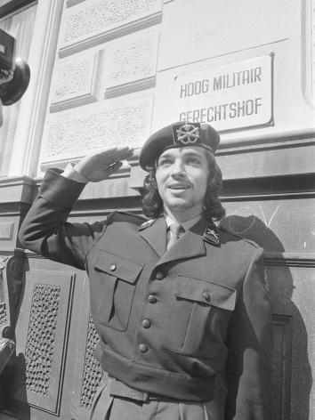 Zwart wit foto van Rinus Wehrmann die met lang haar in uniform salueert