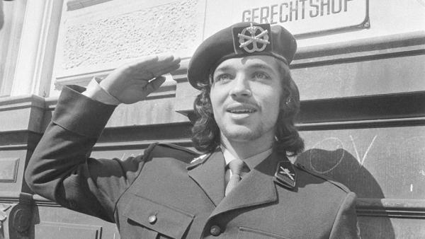 Zwart wit foto van Rinus Wehrmann die met lang haar in uniform salueert