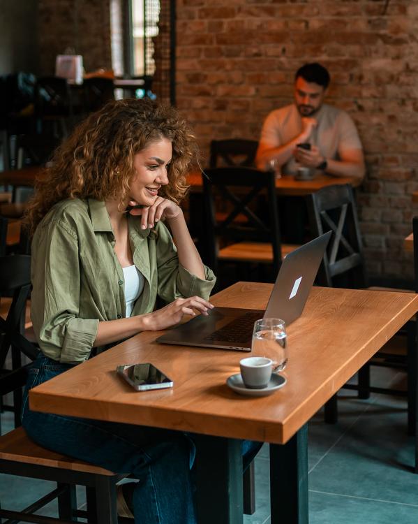 Een vrouw zit aan een tafel in een café op haar laptop