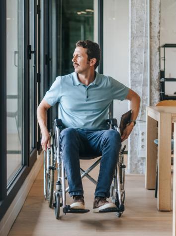 Man rijdt in zijn rolstoel door een gang terwijl hij uit het raam kijkt