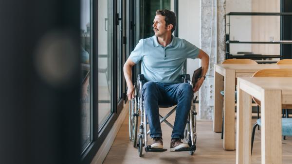Man rijdt in zijn rolstoel door een gang terwijl hij uit het raam kijkt
